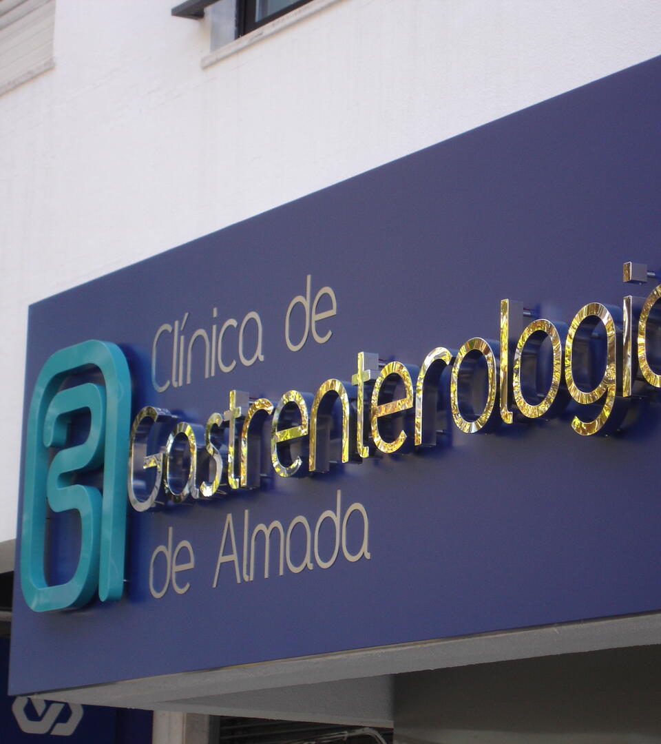Reclamo exterior com letras em relevo de efeito espelhado, aplicadas sobre painel azul. Design moderno e sofisticado com grande impacto visual.