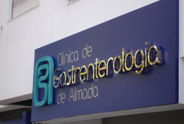 Reclamo exterior com letras em relevo de efeito espelhado, aplicadas sobre painel azul. Design moderno e sofisticado com grande impacto visual.