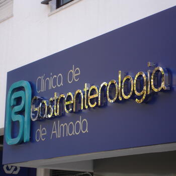 Reclamo exterior com letras em relevo de efeito espelhado, aplicadas sobre painel azul. Design moderno e sofisticado com grande impacto visual.
